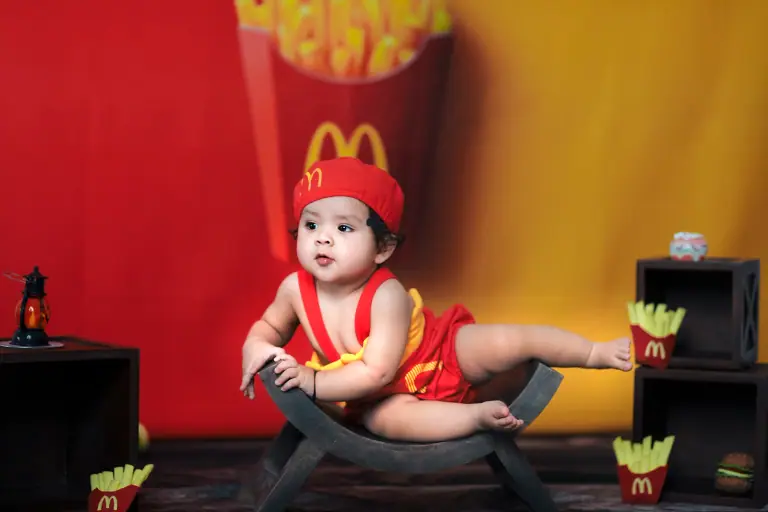 Baby in a red fries-style outfit on a small rocker in a red and yellow fast-food themed set